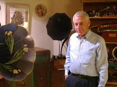 Art Heller standing among antique external-horn phonographs.