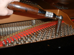 A hand using a tuning lever on the pins and strings inside a piano.